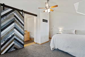 Bedroom featuring lofted ceiling, ceiling fan, a barn door, carpet, and a baseboard heating unit