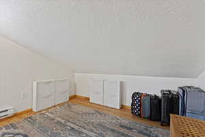 Bonus room with hardwood / wood-style floors, vaulted ceiling, a textured ceiling, and baseboard heating