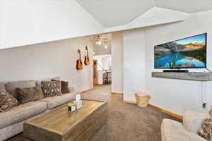 Living room featuring lofted ceiling, a textured ceiling, ceiling fan, and carpet flooring