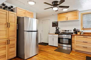 Kitchen with ceiling fan, stainless steel appliances, light hardwood / wood-style floors, a textured ceiling, and light brown cabinetry