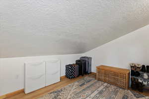 Bonus room with hardwood / wood-style flooring, vaulted ceiling, and a textured ceiling