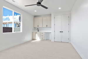 Unfurnished office featuring built in desk, sink, light colored carpet, and ceiling fan