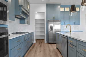 Kitchen with blue cabinetry, sink, decorative light fixtures, light wood-type flooring, and appliances with stainless steel finishes