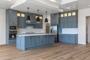 Kitchen featuring blue cabinets, hanging light fixtures, light hardwood / wood-style floors, and appliances with stainless steel finishes