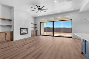 Unfurnished living room featuring ceiling fan, a large fireplace, and light hardwood / wood-style floors