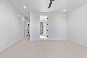 Unfurnished bedroom featuring a walk in closet, light colored carpet, and ceiling fan