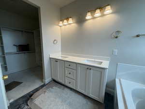 Full bath with double vanity, a washtub, baseboards, a spacious closet, and a sink