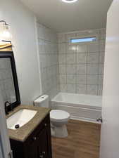 Full bathroom with hardwood / wood-style flooring, tiled shower / bath combo, vanity, a textured ceiling, and toilet