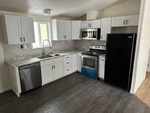 Kitchen with lofted ceiling, sink, stainless steel appliances, decorative backsplash, and white cabinets