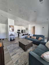 Living room featuring a textured ceiling, visible vents, light wood-type flooring, and baseboards
