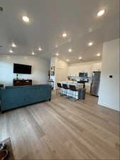 Living room featuring lofted ceiling, sink, light hardwood / wood-style floors, and a textured ceiling