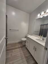 Full bath with toilet, wood finished floors, vanity, and a textured ceiling