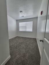 Empty room featuring baseboards, visible vents, dark colored carpet, and a textured ceiling