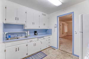 Kitchen with white refrigerator, sink, white cabinets, and a textured ceiling