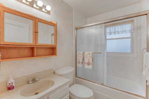 Full bathroom with vanity, shower / bath combination with glass door, and toilet