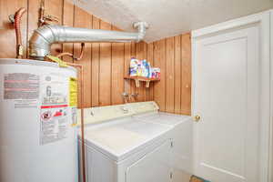 Clothes washing area featuring water heater, washer and dryer, wooden walls, and a textured ceiling