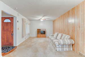 Living room with light colored carpet, a textured ceiling, ceiling fan, and wood walls