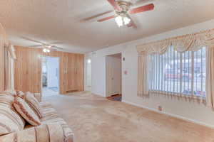 Living room featuring ceiling fan, light carpet, a textured ceiling, and wooden walls