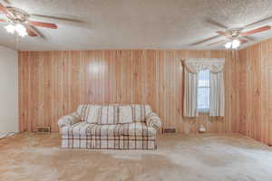 Unfurnished room with carpet floors, ceiling fan, wooden walls, and a textured ceiling