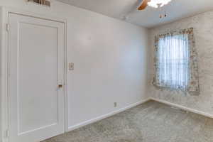 Empty room with ceiling fan, a textured ceiling, and carpet flooring