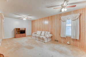 Unfurnished living room with ceiling fan, carpet floors, a textured ceiling, and wood walls