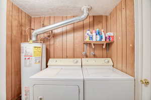 Laundry area featuring washer and dryer, a textured ceiling, water heater, and wood walls