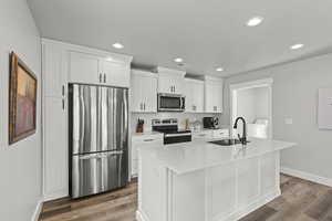 Kitchen featuring appliances with stainless steel finishes, sink, a center island with sink, and white cabinets