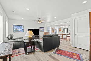 Living room with ceiling fan with notable chandelier and light wood-type flooring