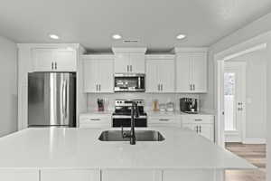 Kitchen with white cabinets, light stone counters, stainless steel appliances, a center island with sink, and light wood-type flooring