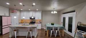 Kitchen featuring sink, white cabinetry, appliances with stainless steel finishes, an island with sink, and pendant lighting