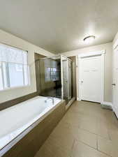 Master bathroom featuring separate shower and tub, tile patterned flooring, and a textured ceiling