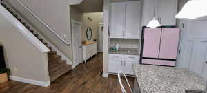 Kitchen featuring light stone counters, white cabinetry, dark wood-type flooring, and fridge