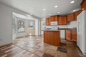 Kitchen featuring white appliances, a kitchen island, and a textured ceiling