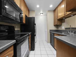 Kitchen featuring sink, light tile patterned floors, and black appliances