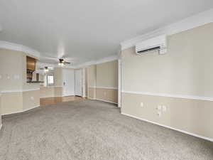 Unfurnished living room featuring crown molding, ceiling fan, carpet flooring, and an AC wall unit