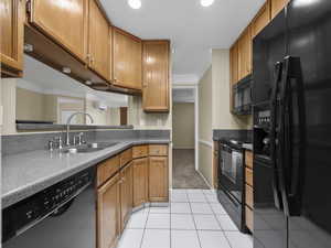 Kitchen with crown molding, sink, light tile patterned floors, and black appliances