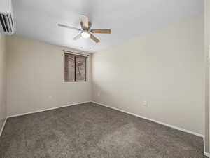 Unfurnished room featuring ceiling fan, a wall mounted air conditioner, and dark carpet