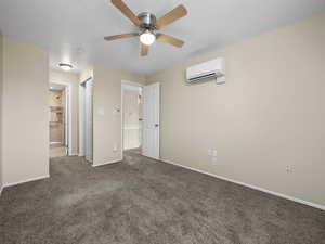 Unfurnished bedroom with ceiling fan, a wall mounted AC, dark carpet, and ensuite bath