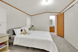 Bedroom featuring vaulted ceiling, light carpet, and ensuite bath