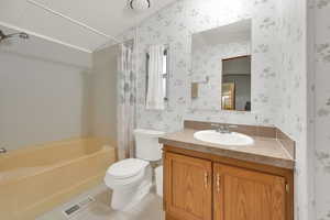 Full master bathroom with tile patterned floors, toilet, vanity, and shower / bathtub combination with curtain