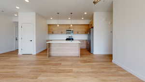 Kitchen featuring hanging light fixtures, an island with sink, stainless steel appliances, and light wood-type flooring