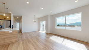 Unfurnished living room featuring a water and mountain view, light hardwood / wood-style flooring, sink, and a chandelier