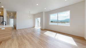 Unfurnished living room with a water view, sink, light hardwood / wood-style floors, and an inviting chandelier