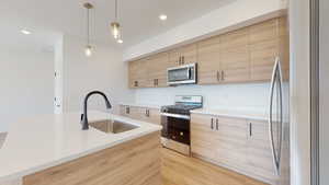 Kitchen with a center island with sink, light brown cabinetry, stainless steel appliances, pendant lighting, and sink