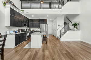 Kitchen with appliances with stainless steel finishes, a kitchen breakfast bar, a center island, light stone countertops, and light wood-type flooring