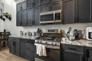 Kitchen featuring stainless steel appliances, light stone counters, and light hardwood / wood-style floors