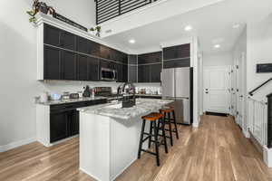 Kitchen with light hardwood / wood-style flooring, appliances with stainless steel finishes, a kitchen breakfast bar, light stone counters, and an island with sink