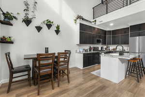 Kitchen with appliances with stainless steel finishes, an island with sink, sink, light stone counters, and light hardwood / wood-style flooring