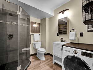 Bathroom with toilet, a shower with shower door, hardwood / wood-style floors, washer / clothes dryer, and vanity