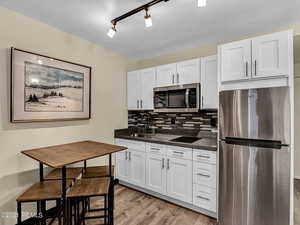 Kitchen featuring light hardwood / wood-style flooring, sink, backsplash, white cabinetry, and stainless steel appliances